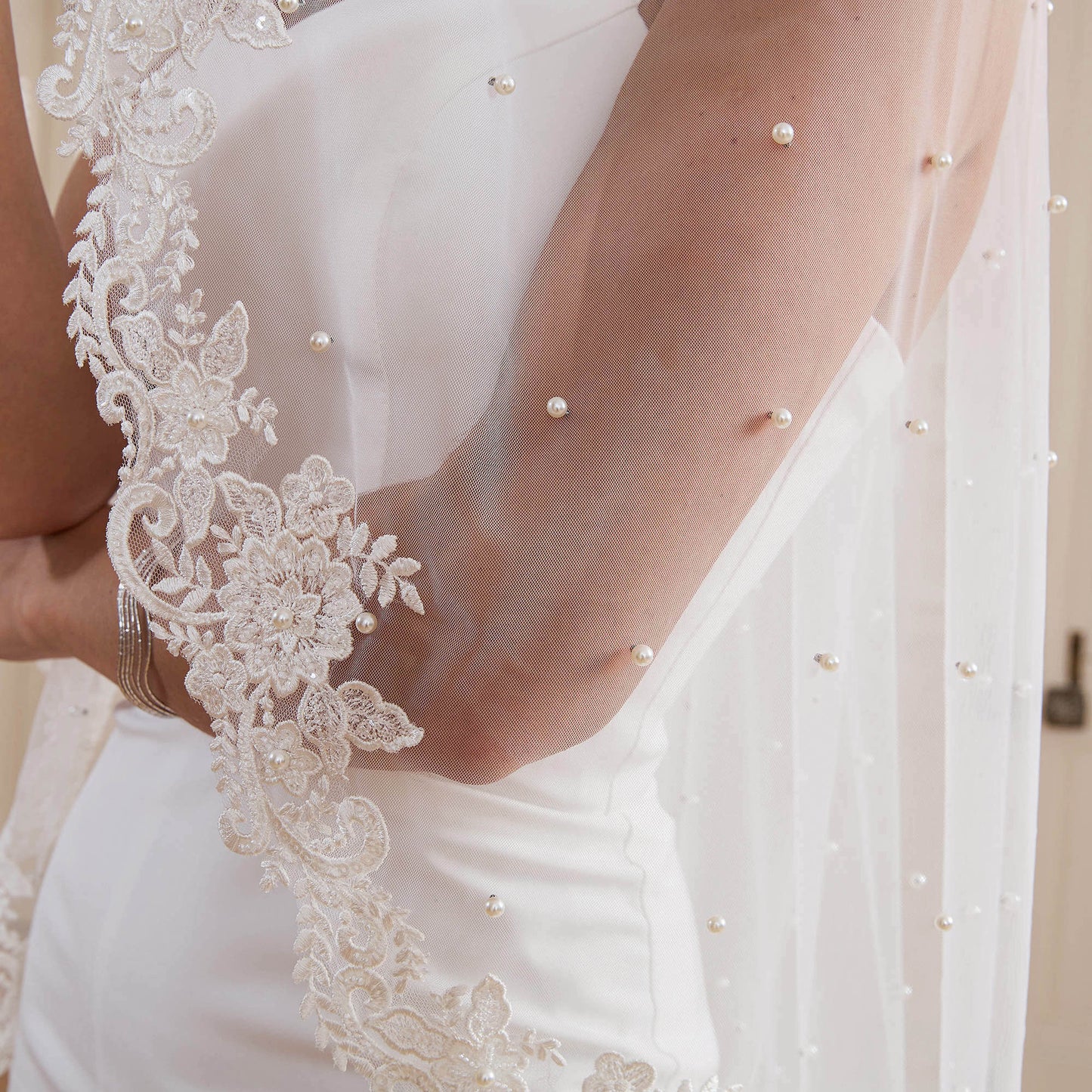 Close-up of 6mm pearls and glass beaded lace edge on soft tulle draped over arm Nicola Xu Atelier