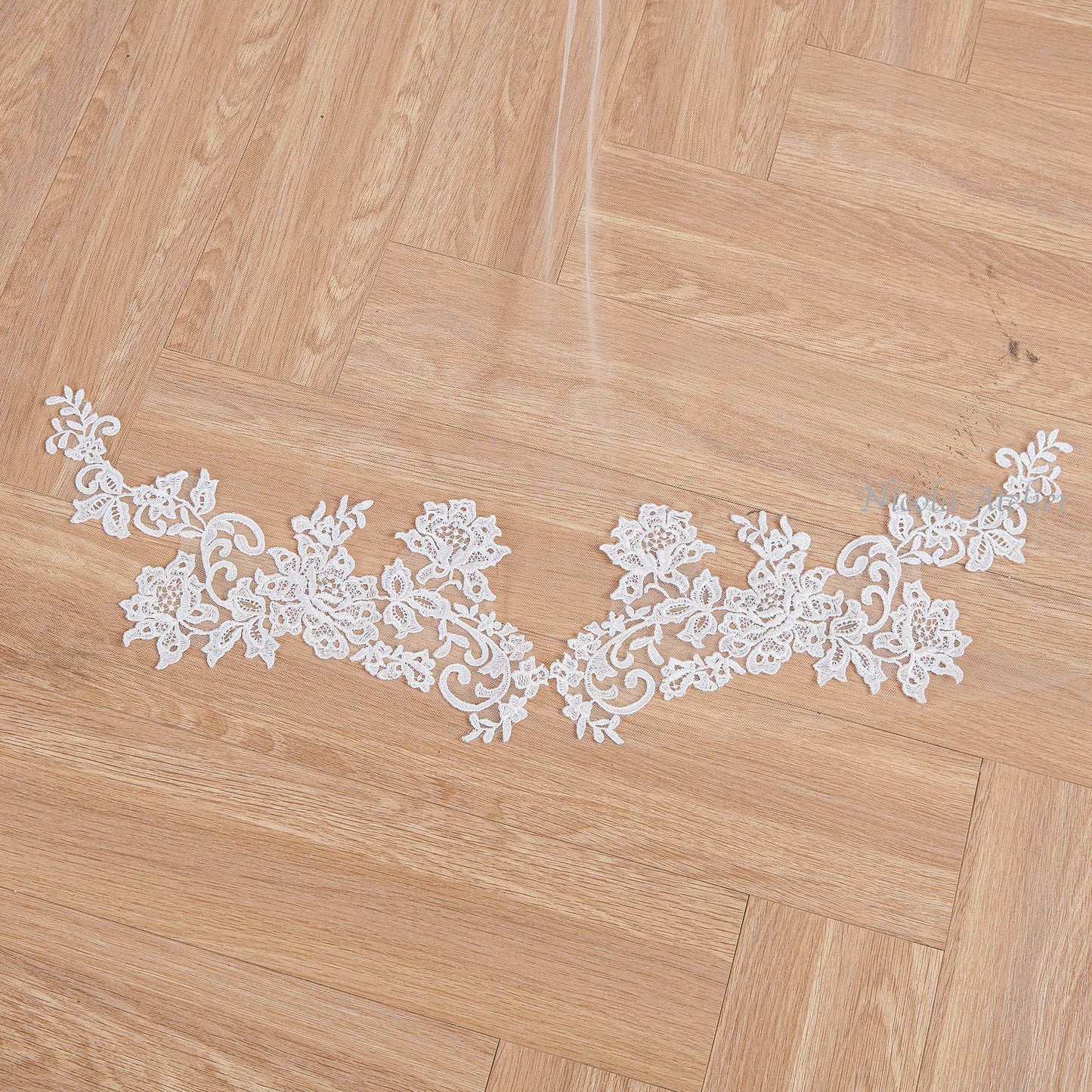 Close-up of floral lace applique with hand-sewn details on wooden floor. Nicola Xu Atelier.
