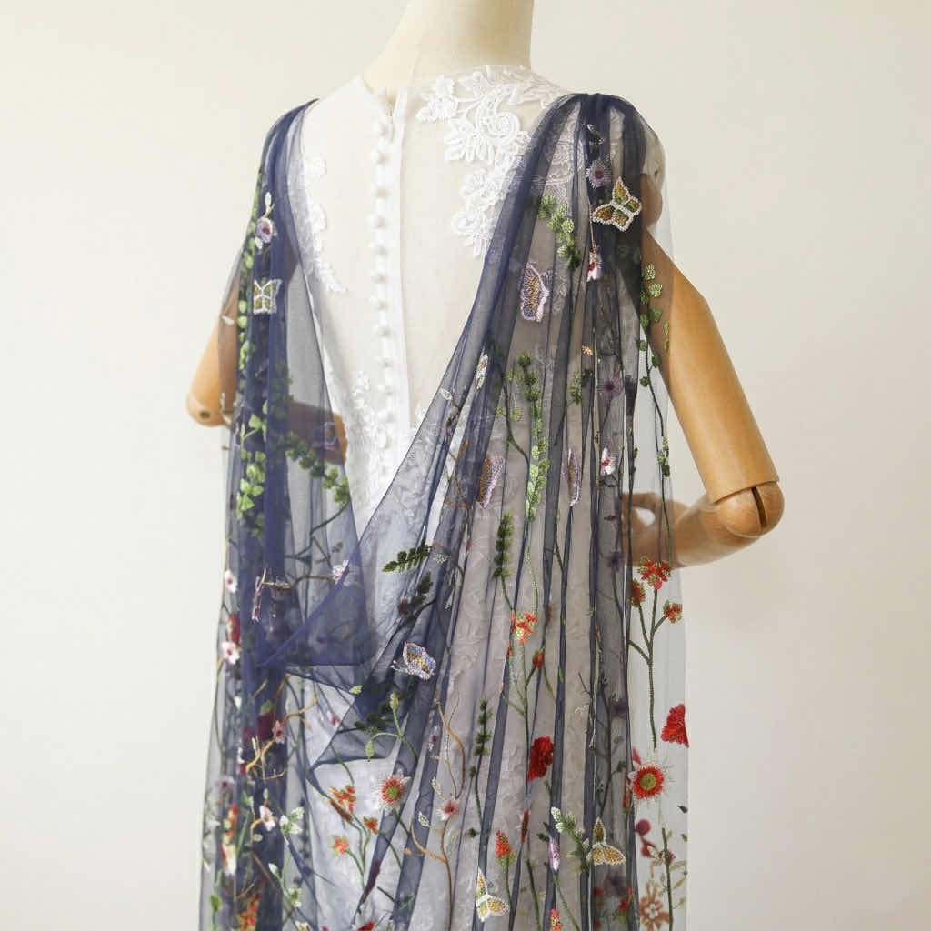 Angled view showing detachable shoulder attachments of a navy floral embroidered tulle drape on a dress form.