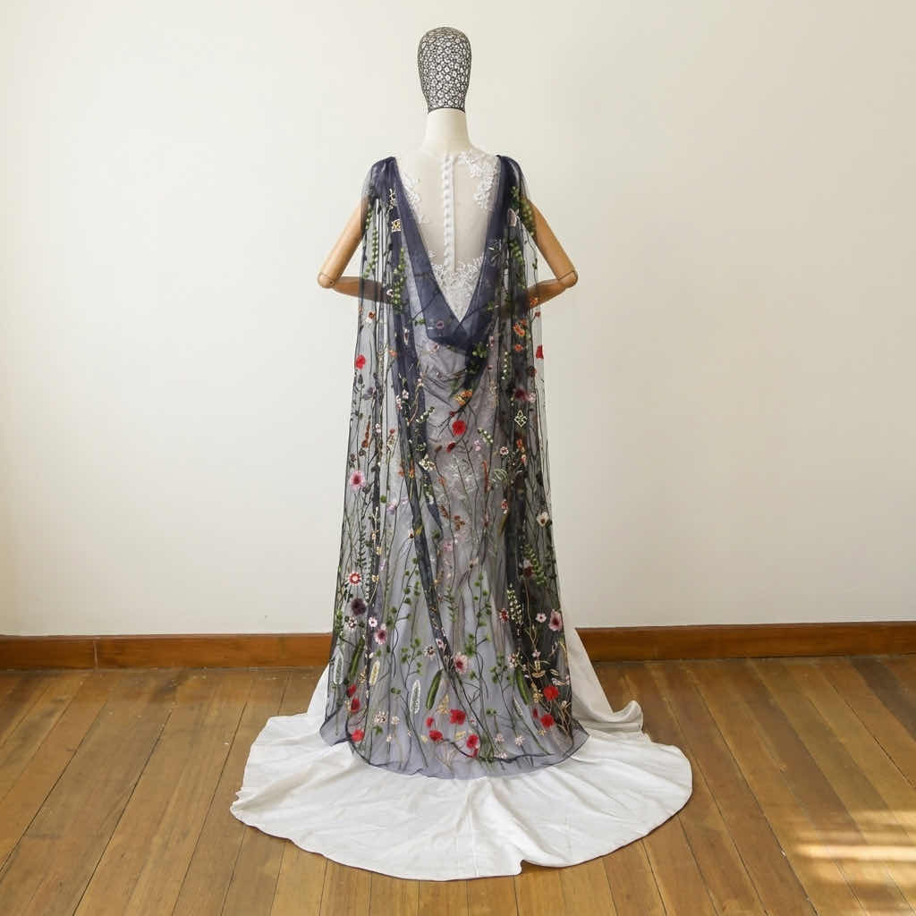 Back view of an ankle-length navy blue mesh veil featuring embroidered red flowers and green vines on a mannequin.