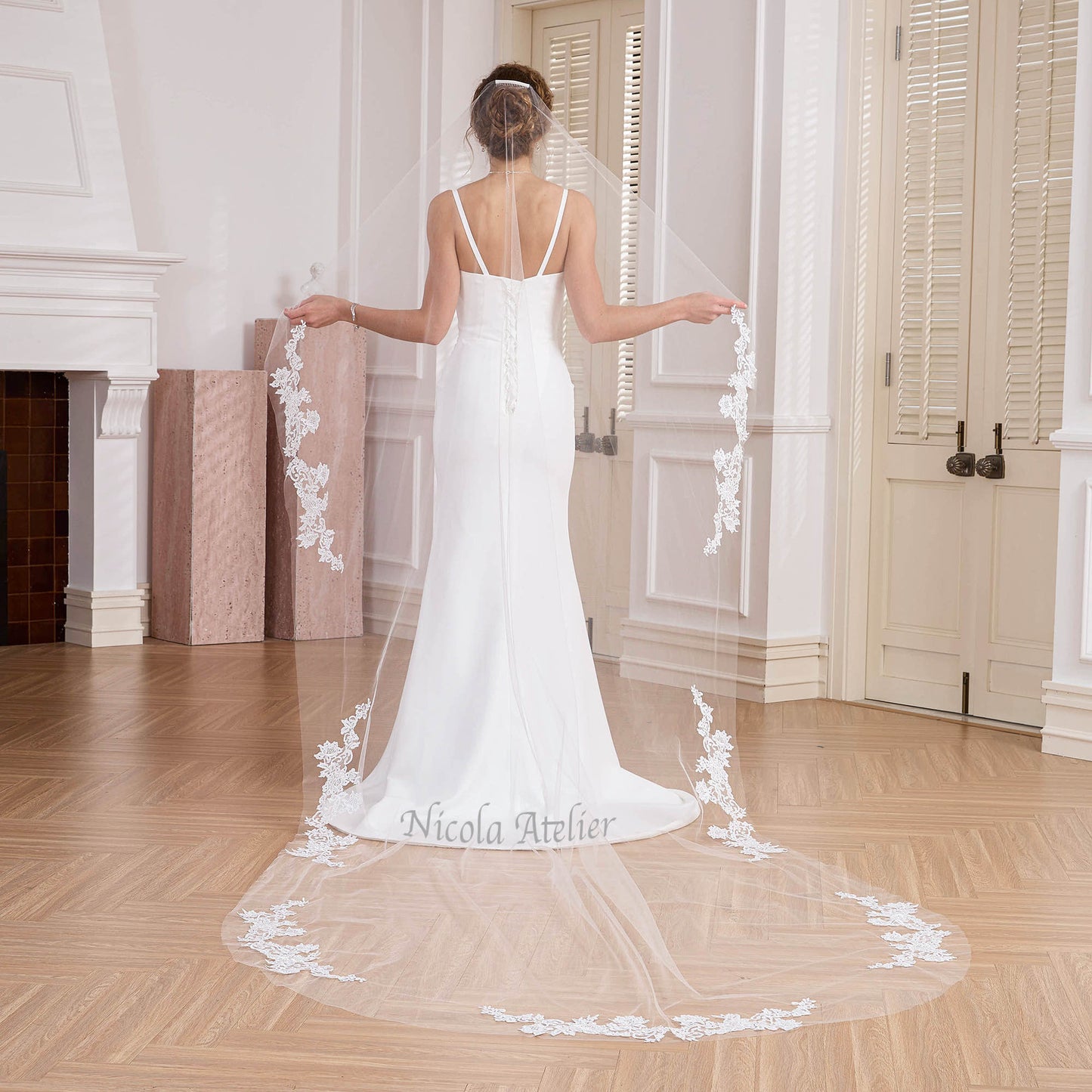 Back view of bride holding out narrow cathedral veil with lace edge in studio. Nicola Xu Atelier.