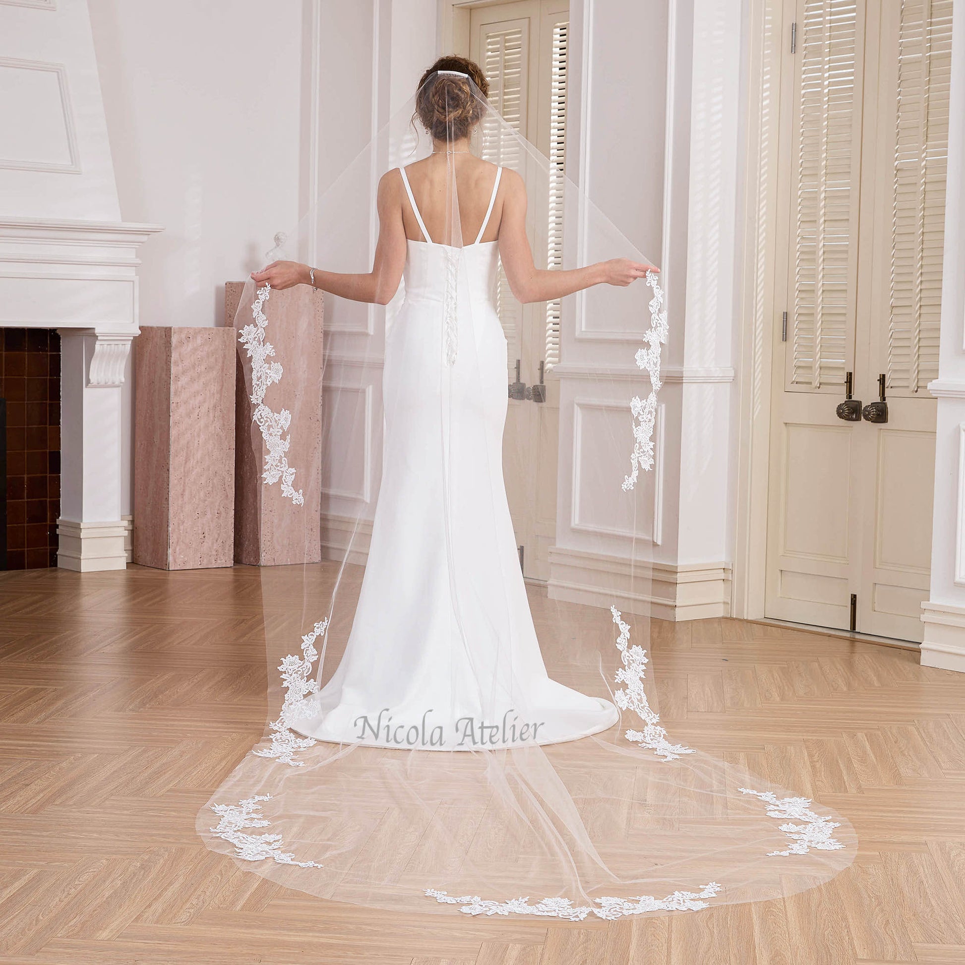 Back view of bride holding out narrow cathedral veil with lace edge in studio. Nicola Xu Atelier.