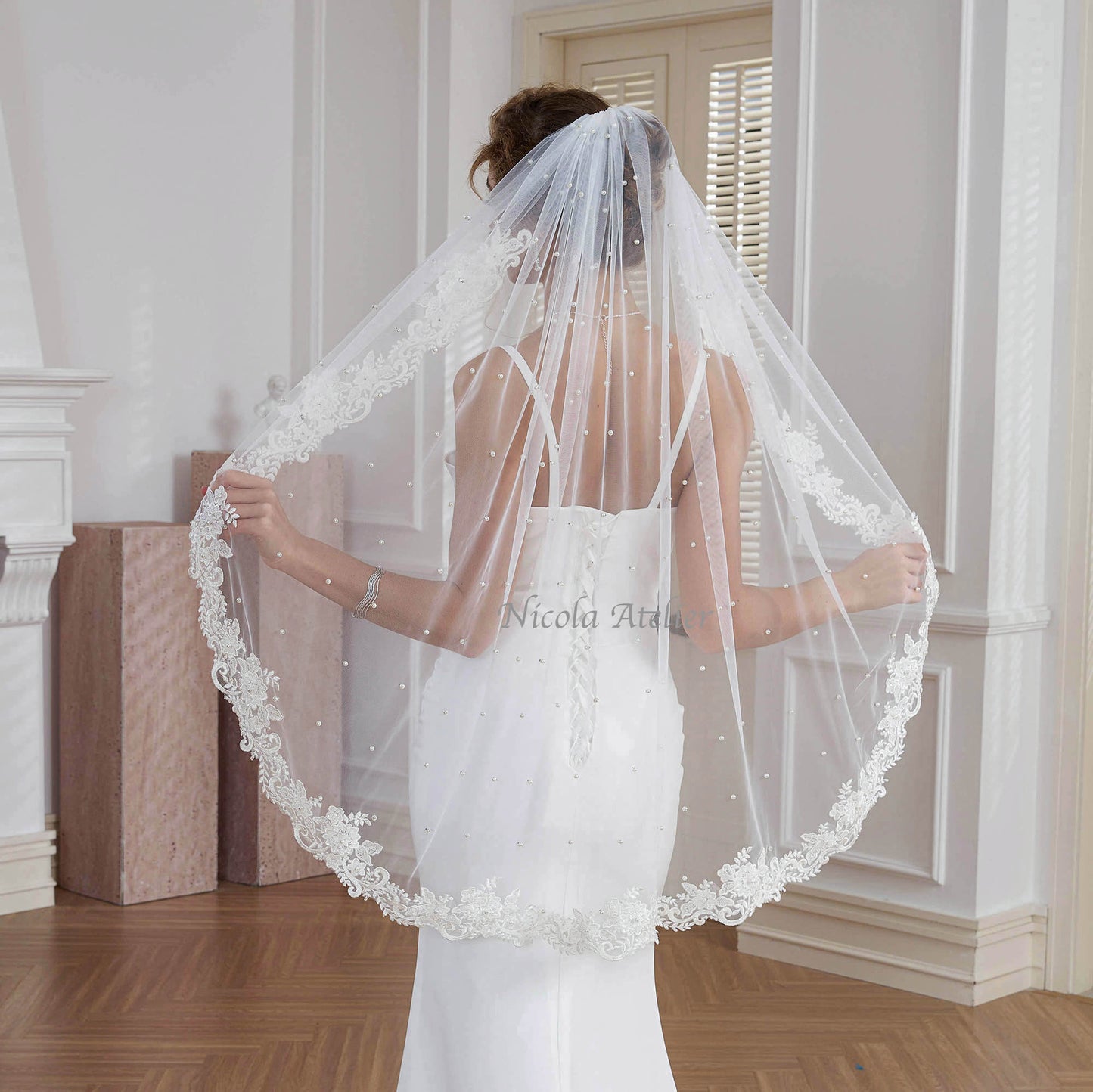 Back view of bride spreading out sheer tulle veil showing full scalloped beaded lace edge Nicola Xu Atelier
