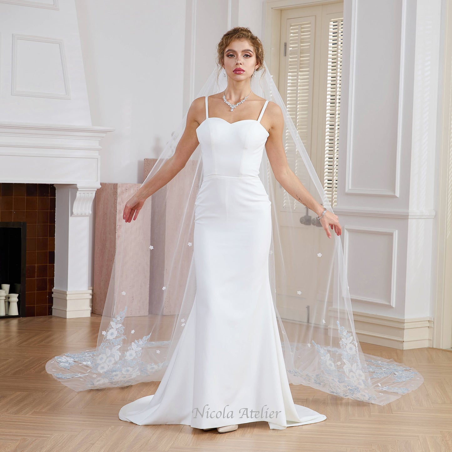 Bride facing forward holding sheer tulle veil with light blue floral edge. Indoor studio setting. Nicola Xu Atelier.