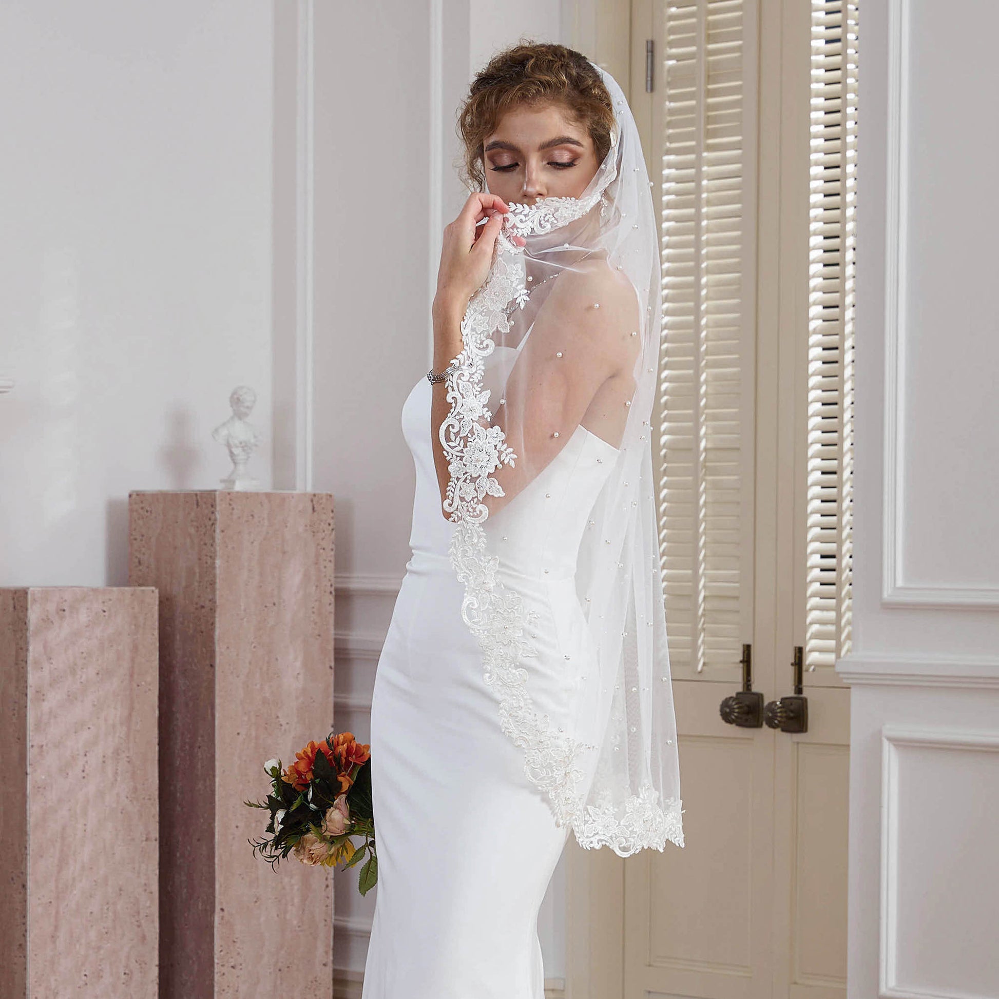 Bride holding pearl and glass beaded lace veil edge near face in natural light studio Nicola Xu Atelier