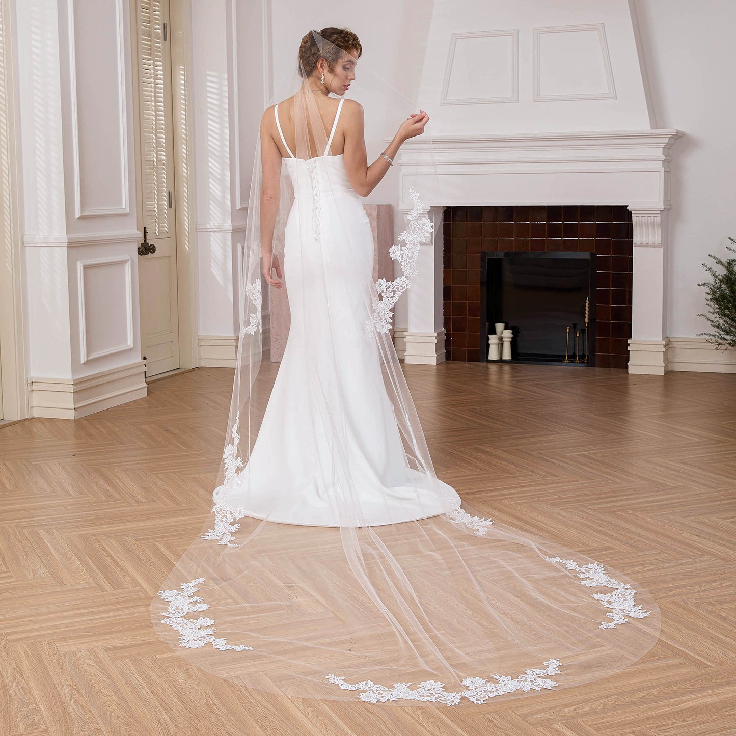 Bride looking over shoulder wearing a single-tier cathedral veil with lace border in an elegant room. Nicola Xu Atelier.