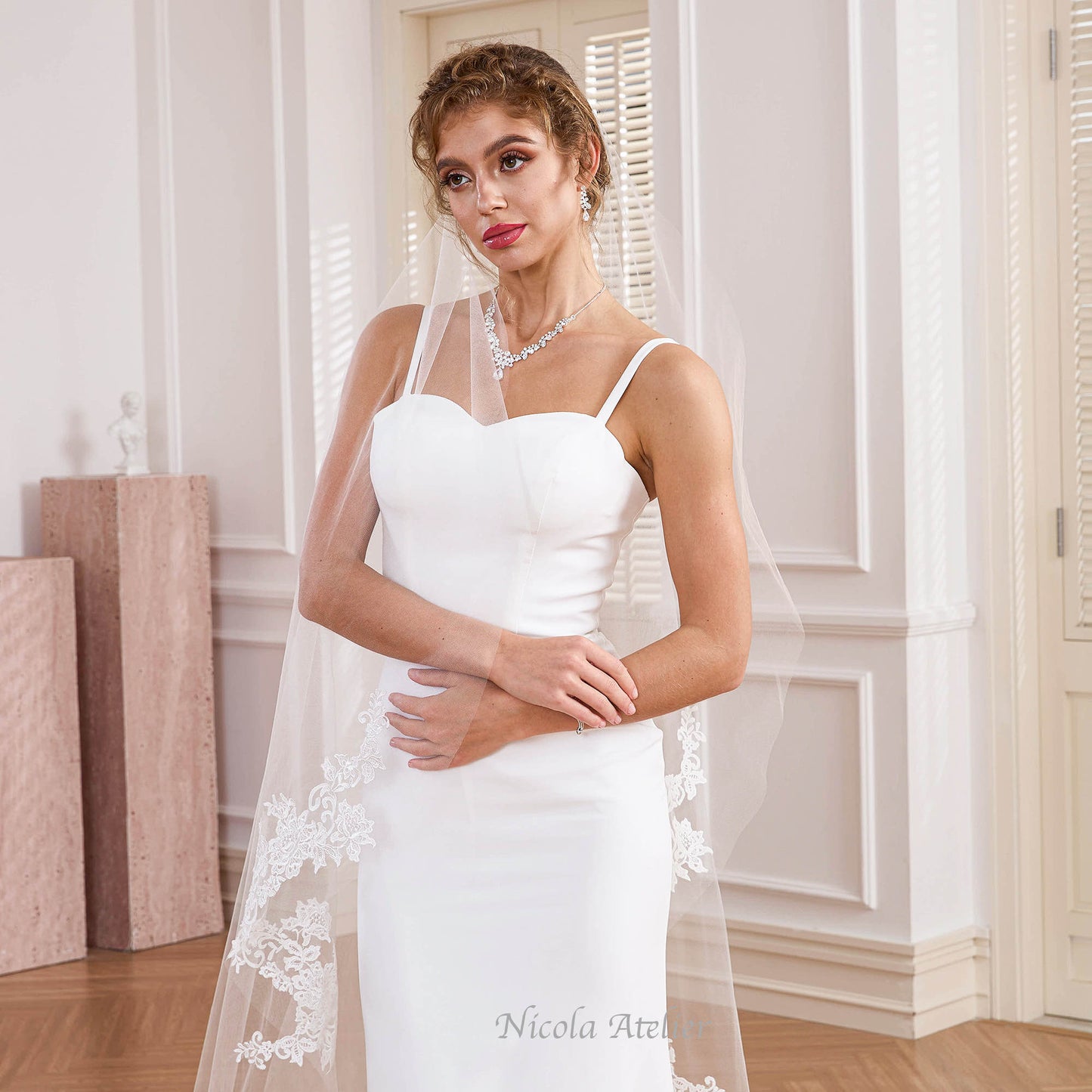 Bride looking sideways wearing narrow sheer tulle veil in white room. Nicola Xu Atelier.