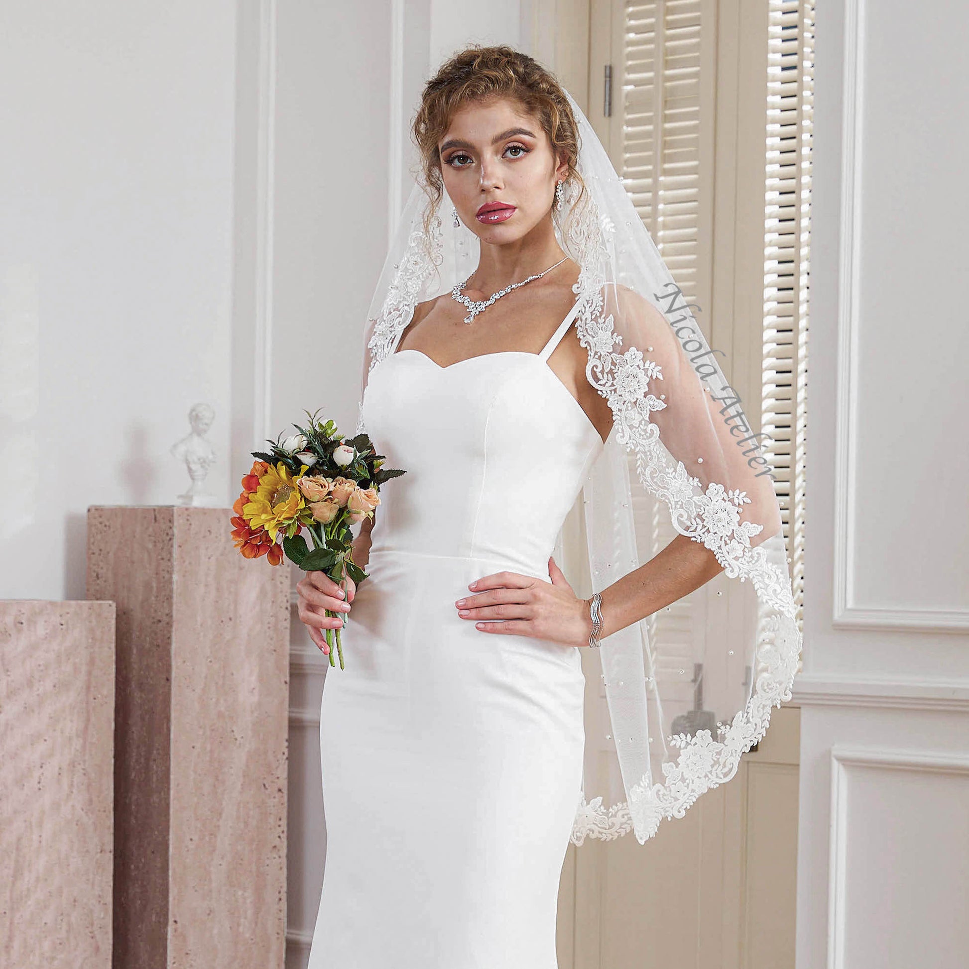 Bride with hand on hip wearing pearl beaded lace veil holding fall bouquet in elegant room Nicola Xu Atelier