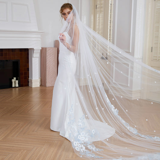 Bride wrapped in sheer bridal veil highlighting hand-sewn light blue 3D floral lace. Indoor scene. Nicola Xu Atelier.