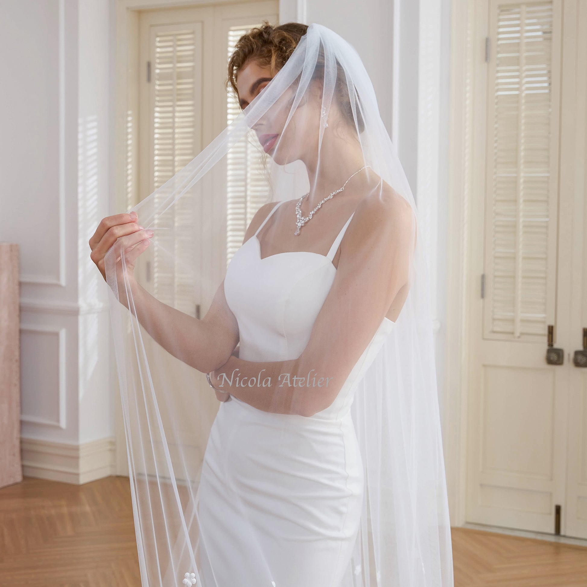 Close-up of bride holding soft tulle veil near face showing delicate sheer fabric. Studio setting. Nicola Xu Atelier.