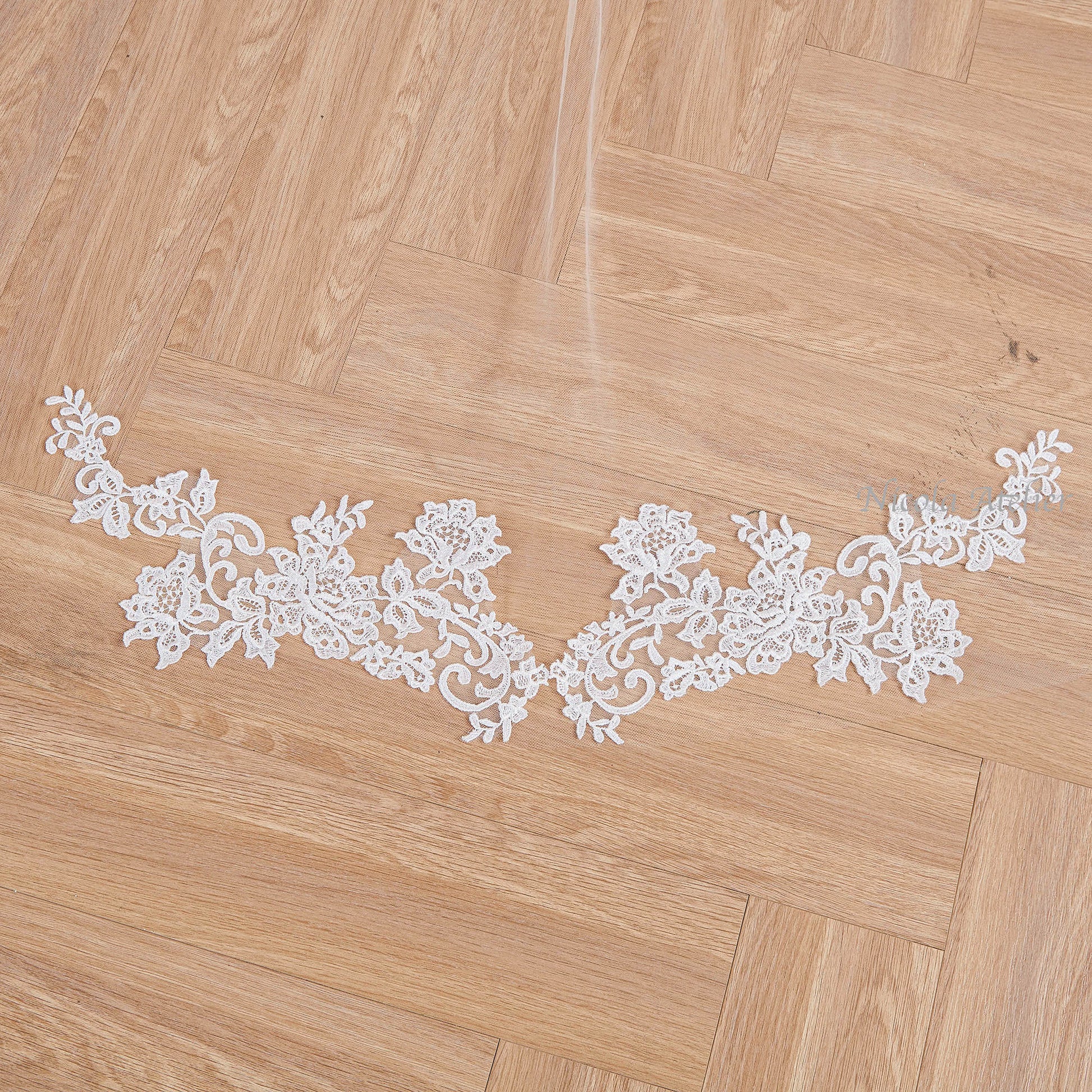 Close-up of floral lace applique with hand-sewn details on wooden floor. Nicola Xu Atelier.