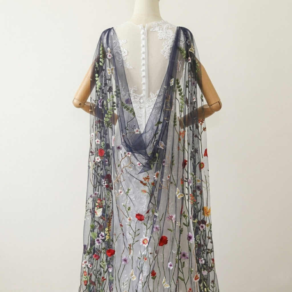 Close up of colorful embroidered butterflies and wildflowers on a dark sheer Watteau veil draped on a mannequin