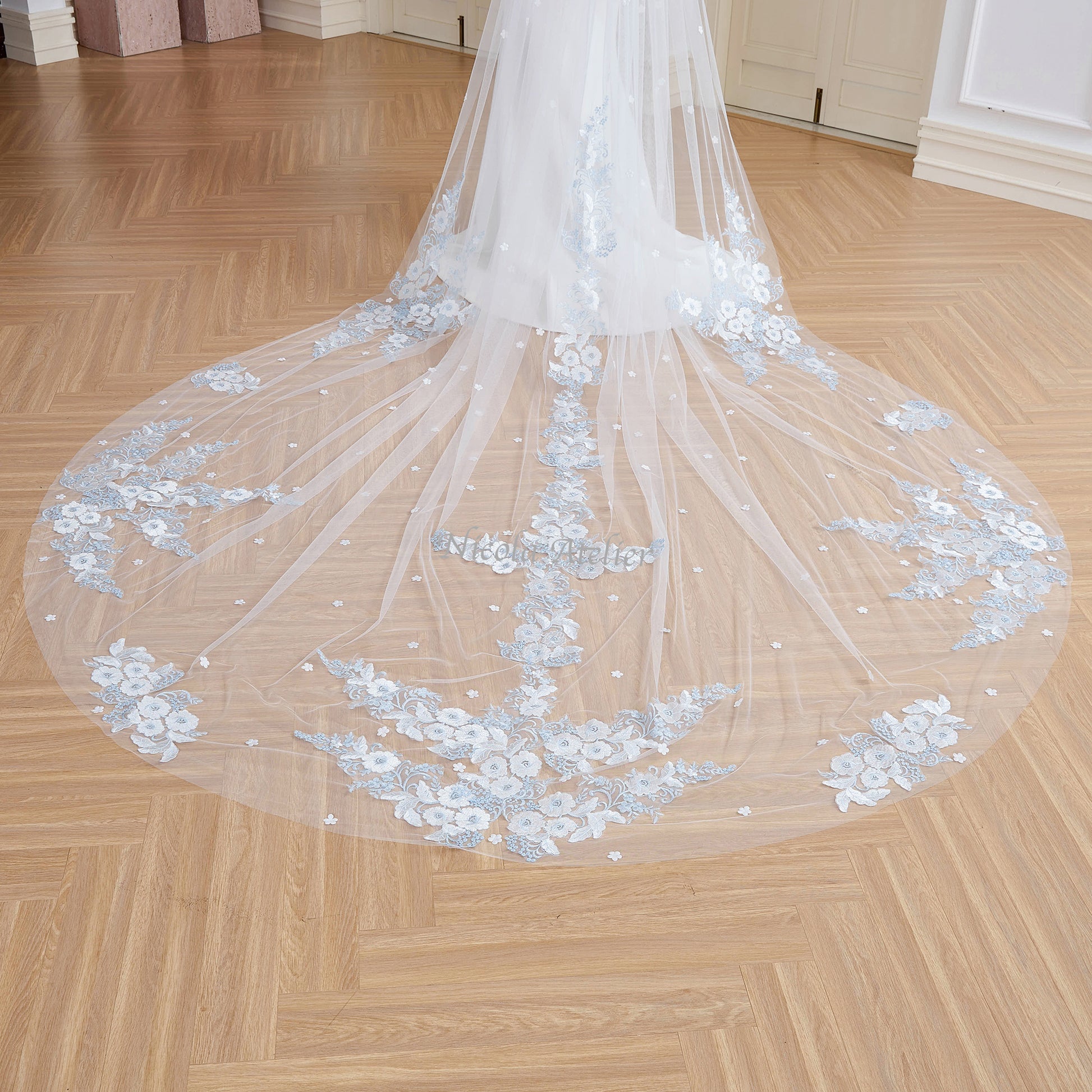 Detailed view of veil train on floor featuring light blue and ivory center lace motif. Indoor studio. Nicola Xu Atelier.