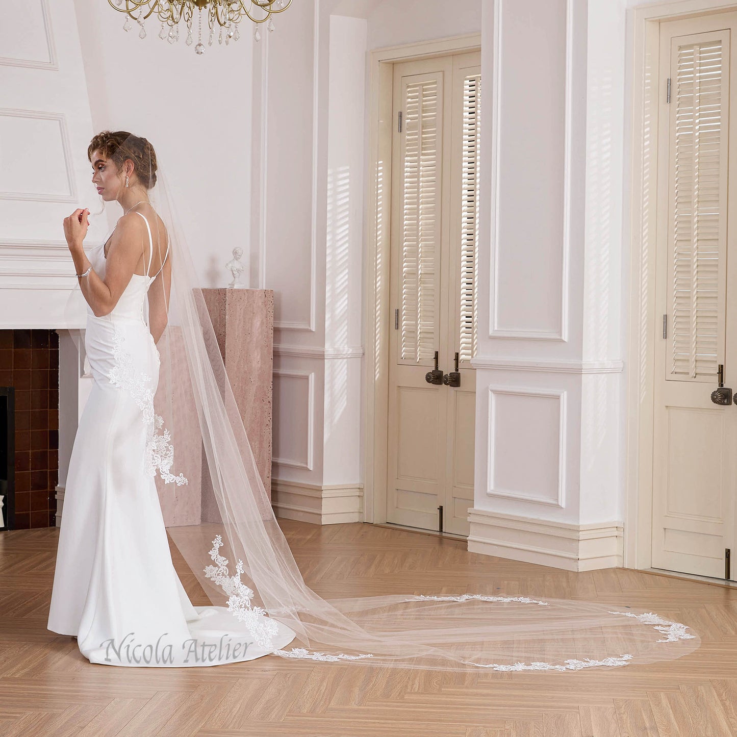 Side profile of bride with trailing sheer cathedral veil and lace edge in elegant room. Nicola Xu Atelier.